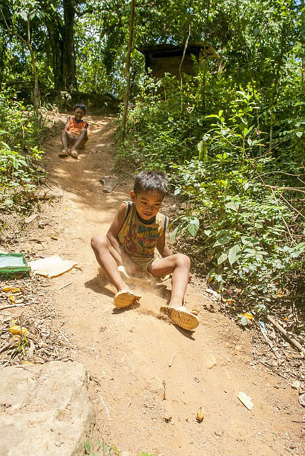 Ở vùng miền núi cao hẻo lánh xa xôi phía tây Quảng Bình, cuộc sống tinh thần của các em nhỏ còn thiếu thốn đủ bề, ngoài tivi ra thì không có điểm vui chơi giải trí mang tính cộng đồng nào. Cậu bé nghĩ ra trò chơi trượt tuyết, đường trượt là con dốc trước nhà ông trưởng bản, máng trượt được làm từ chiếc can nhựa đã hỏng và mấy mo cau già - Ảnh: Phạm Văn Thức