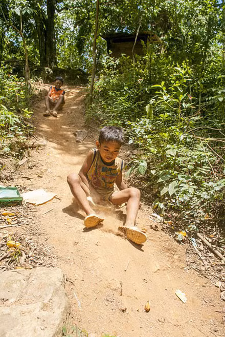Ở vùng miền núi cao hẻo lánh xa xôi phía tây Quảng Bình, cuộc sống tinh thần của các em nhỏ còn thiếu thốn đủ bề, ngoài tivi ra thì không có điểm vui chơi giải trí mang tính cộng đồng nào. Cậu bé nghĩ ra trò chơi trượt tuyết, đường trượt là con dốc trước nhà ông trưởng bản, máng trượt được làm từ chiếc can nhựa đã hỏng và mấy mo cau già - Ảnh: Phạm Văn Thức