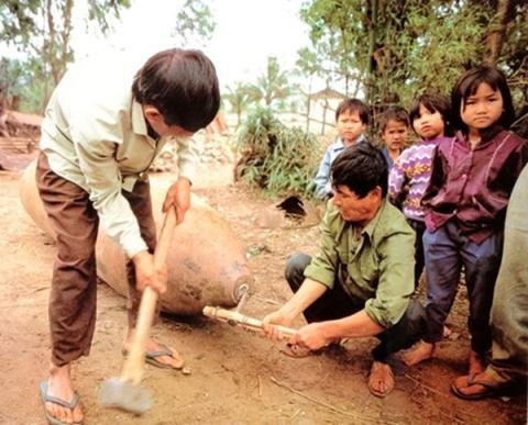 Những con số khủng khiếp đó khiến bất cứ ai trong chúng ta cũng phải giật mình nhưng không ngăn được hàng ngàn người đang hàng ngày thu lượm bom mìn để mưu sinh. Chỉ vì một chút lợi ích trước mắt mà quên đi hậu quả lâu dài thậm chí là vĩnh viễn. Ảnh: Hai người đàn ông đang cố phá một quả bom trong khi bên cạnh họ còn có vô số cháu nhỏ đứng xem vì hiếu kỳ. Nguồn: Lao Động