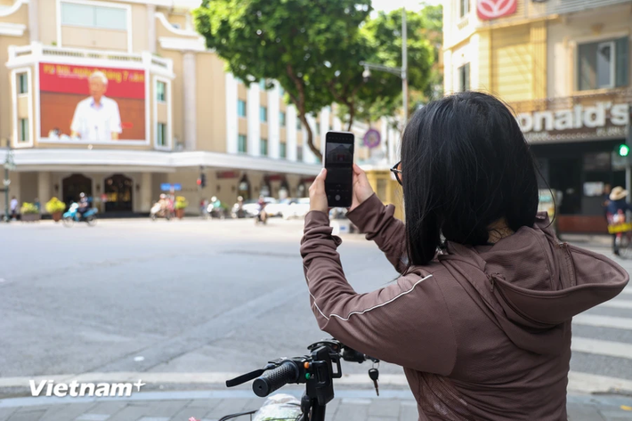 Một người dân đang đứng ghi lại hình ảnh của Tổng Bí thư Nguyễn Phú Trọng trên tấm màn LeD của một trung tâm thương mại phố Tràng Tiền. (Ảnh: Minh Hiếu/vietnam+)