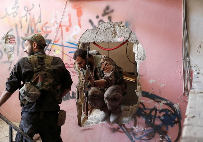 Các thành viên của Lực lượng Dân chủ Syria chui qua một lỗ hổng đục qua tường khi chiến lĩnh vị trí chiến đấu với phiến quân IS bám trụ trong sân vận động Raqqa. Ảnh: REUTERS