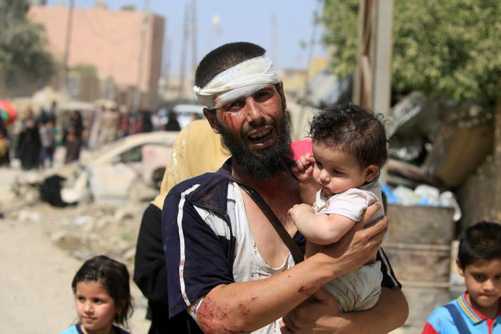 Một người đàn ông cư dân Mosul bị thương bế con sau khi chạy khỏi khu vực do phiến quân IS kiểm soát ở Tây Mosul. Ảnh: REUTERS
