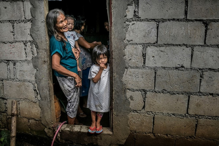 Remy Fernandez, 84 tuổi, bế đứa cháu nội của bà tại nhà ở Patayas, Manila. Fernandez hiện là người nuôi dưỡng 7 đứa cháu sau khi con trai bà, Constantino de Juan, bị giết trong cuộc chiến chống ma túy ở Philippines. Mẹ của những đứa nhỏ hiện chịu án tù giam do buôn bán ma túy. Ảnh: Guardian.