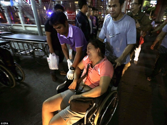 Một người phụ nữ khóc trên xe lăn và được đưa ra khỏi hiện trường vụ nổ bom, trong khi đám đông tụ tập gần nơi xảy ra vụ nổ.