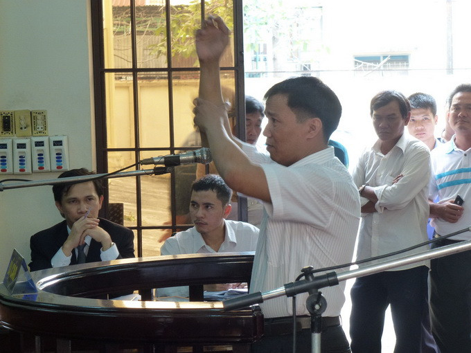 Bị cáo Vinh diễn lại cảnh bị nhiều người nhóm ông Sơn khống chế. Vinh khai, dù nhiều người cùng chụp khẩu súng nhưng Vinh vẫn rút được súng lên bắn chỉ thiên. "Lúc này nhiều người vẫn ập vào đè đánh tôi. Sau khi súng nổ 1-2 phát thì không biết có ai bị thương không. Những viên đạn sau không phải do tôi bắn", Vinh nói và cho hay trong lúc bị đè dưới đất, rất mệt, thì vẫn nghe tiếng súng nổ. Ảnh: Tuổi Trẻ.