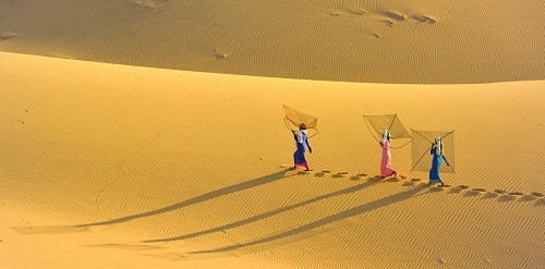 Phụ nữ miền biển Việt Nam bước từng bước qua bãi cát nắng cháy, gió rát để mang cá ra chợ bán.