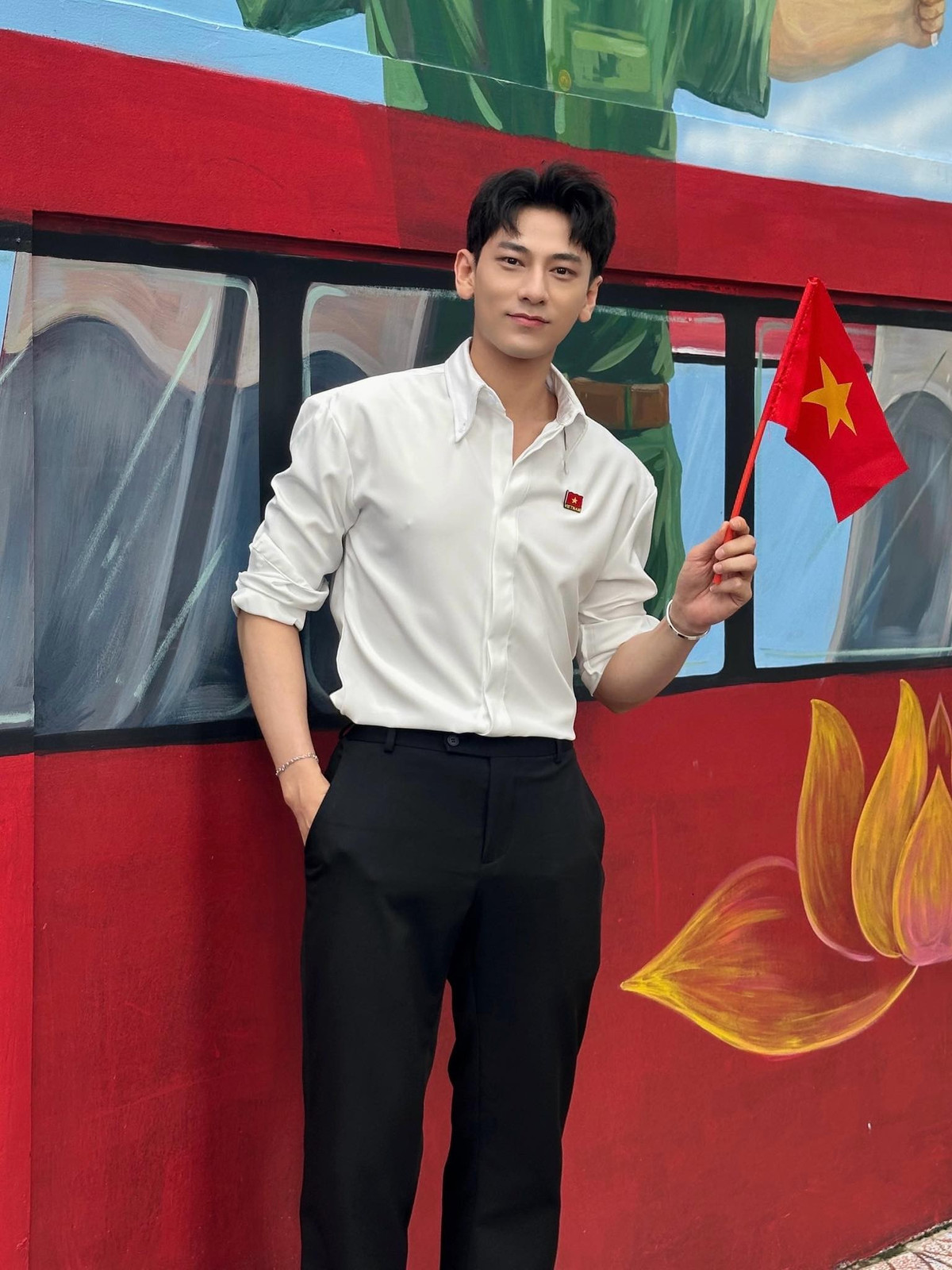 Isaac diện áo sơ mi trắng lịch lãm, cầm cờ đỏ sao vàng chụp ảnh. Ảnh: FB Isaac