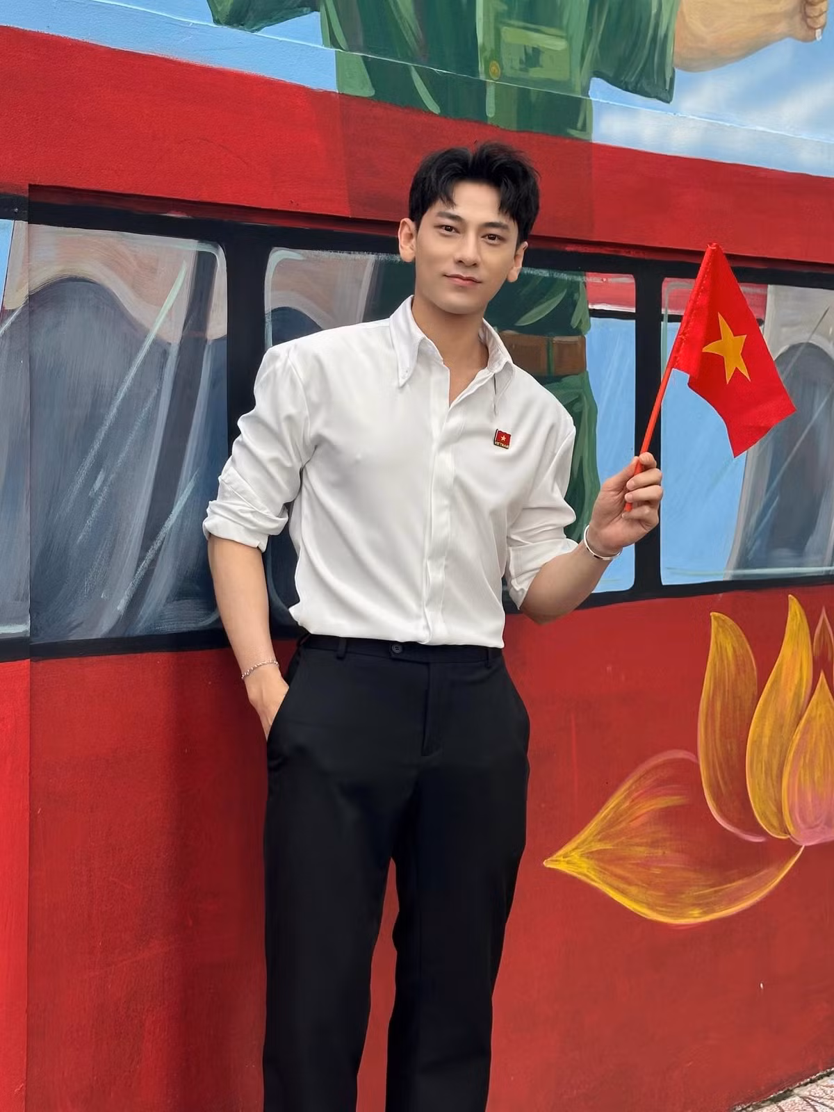 Isaac diện áo sơ mi trắng lịch lãm, cầm cờ đỏ sao vàng chụp ảnh. Ảnh: FB Isaac