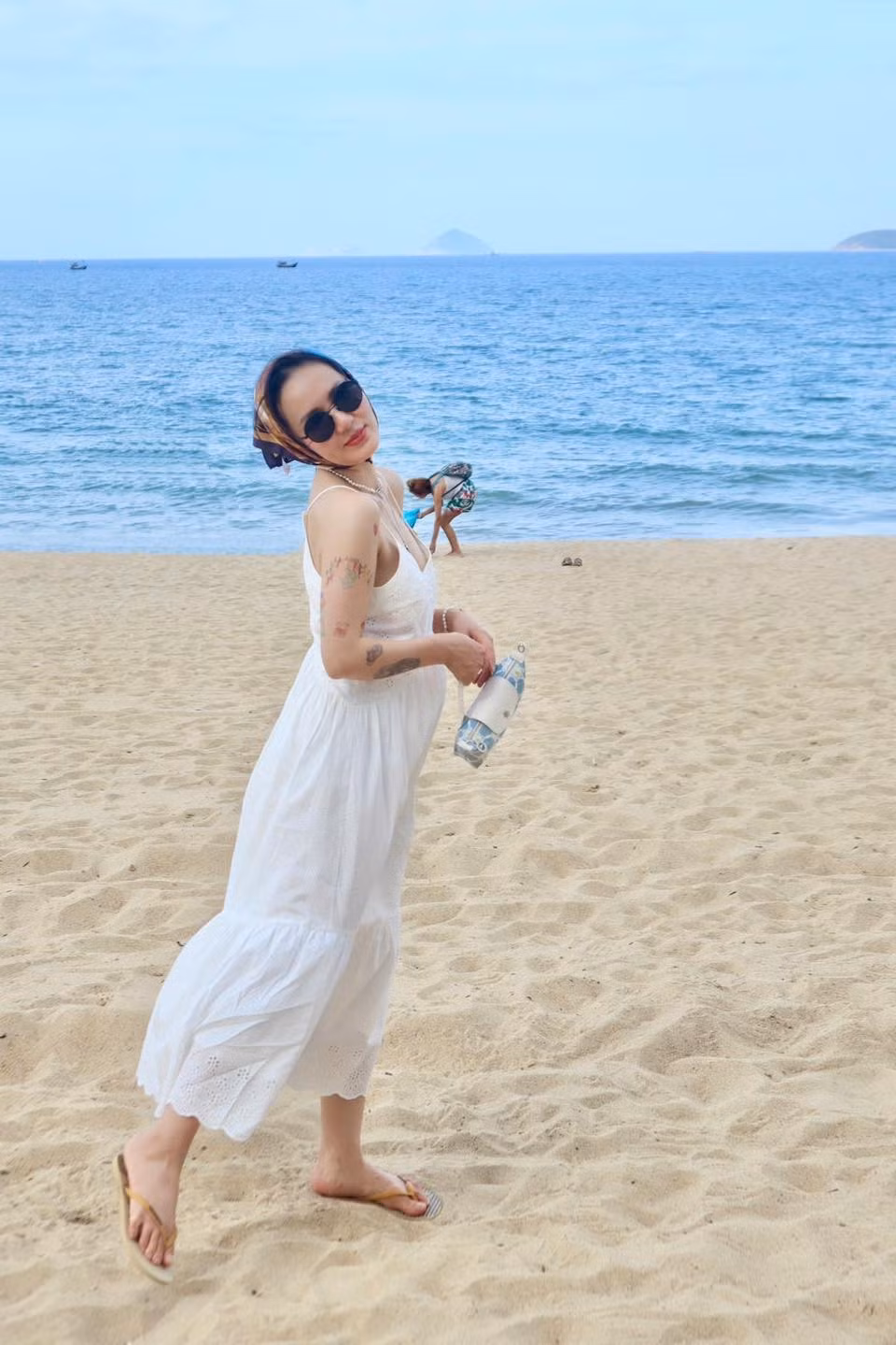 Trong khung cảnh nắng vàng biển xanh, nữ ca sĩ chọn diện váy hai dây màu trắng với chất liệu mỏng nhẹ, tôn lên bờ vai thanh mảnh, thềm ngực gợi cảm cùng vóc dáng cân đối. Ảnh: FB Tran Phuong Linh