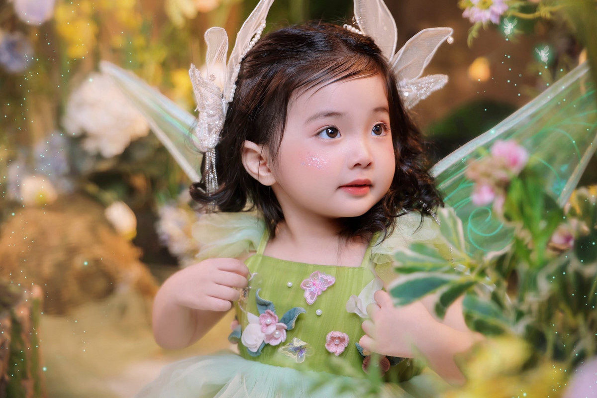 Trong loạt hình, bé Lisa diện váy xòe bồng bềnh, đeo cánh thiên thần tông xanh dịu mát, mái tóc xoăn lọn nhỏ càng làm nổi bật vẻ đáng yêu như một nàng công chúa bước ra từ truyện cổ tích.