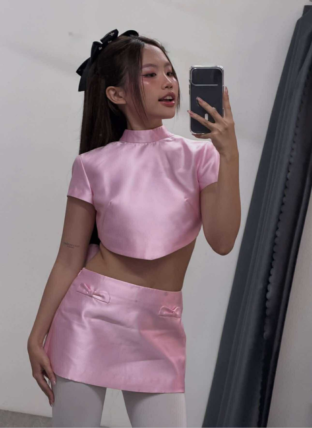 Cô phối cùng tất trắng, giày cao gót và kiểu tóc buộc nửa điểm thêm hai chiếc nơ đen nhỏ tạo nên vẻ ngoài vừa tinh nghịch vừa thanh lịch.