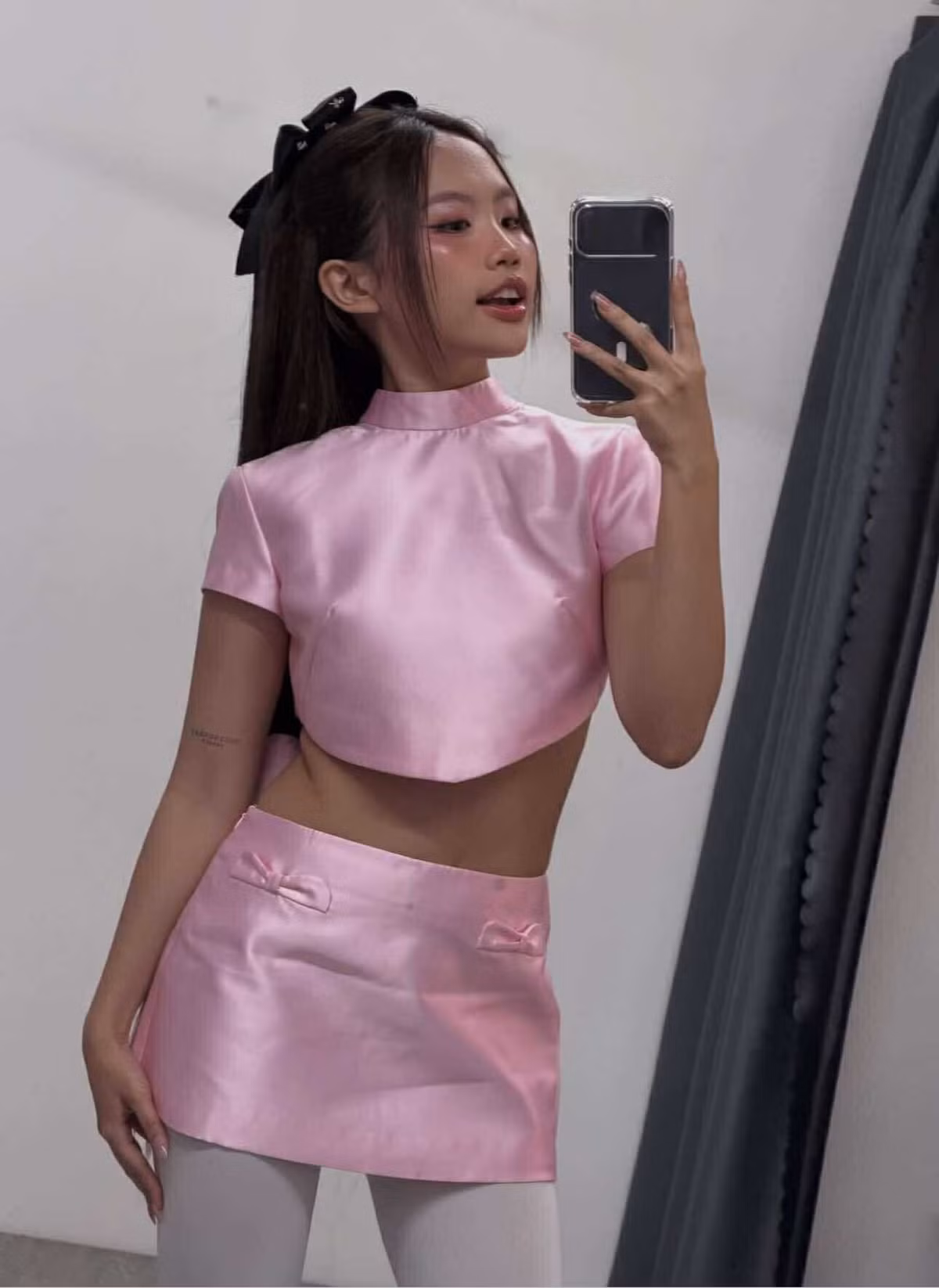 Cô phối cùng tất trắng, giày cao gót và kiểu tóc buộc nửa điểm thêm hai chiếc nơ đen nhỏ tạo nên vẻ ngoài vừa tinh nghịch vừa thanh lịch.