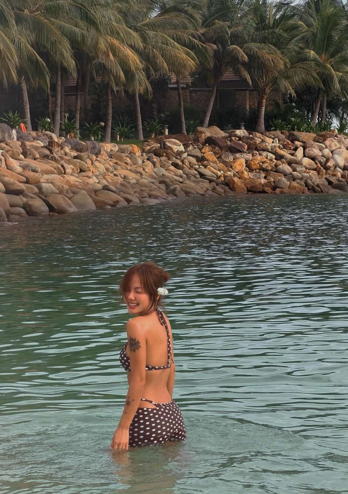 Giữa khung cảnh biển xanh và nắng vàng rực rỡ, nữ ca sĩ lựa chọn bộ đồ tắm hai mảnh họa tiết chấm bi cổ điển, tôn lên trọn vẹn đường cong cơ thể cùng làn da nâu khỏe khoắn.