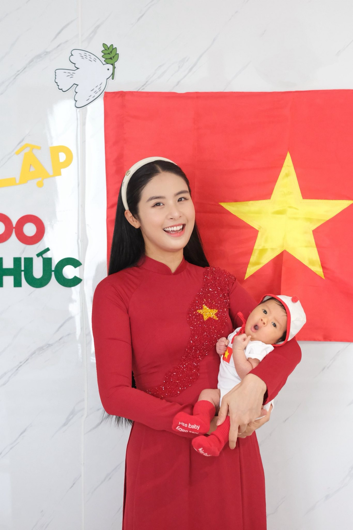 Hoa hậu Ngọc Hân diện áo dài đỏ, bế con trai chụp hình mừng kỷ niệm 71 năm Ngày Giải phóng Thủ đô (10/10/1954 - 10/10/2025). Ảnh: FB Ngoc Han Dang