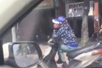 Người phụ nữ ngồi vắt chéo chân, nghe điện thoại khi đang đi xe máy