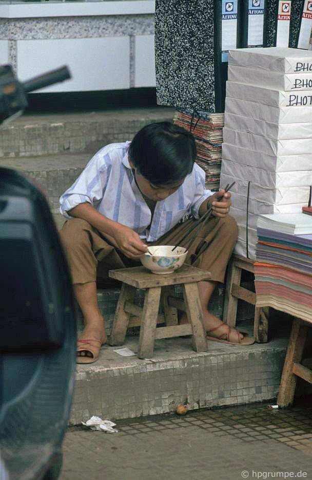 Một cậu bé ngồi ăn cạnh quầy bán giấy photo ở TP HCM.
