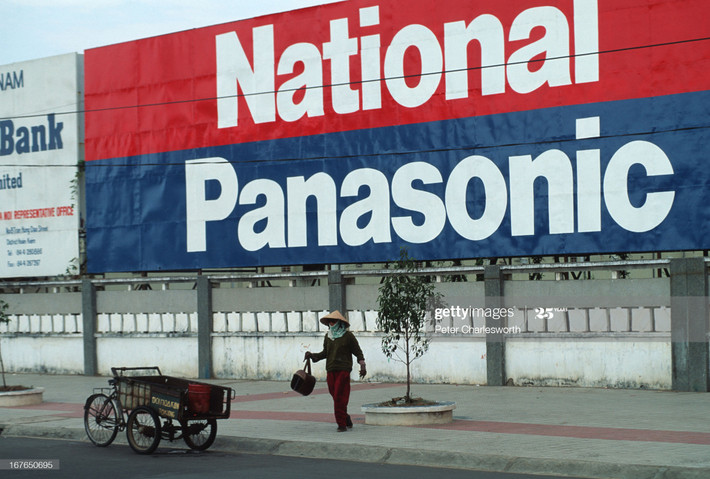 Người phụ nữ và chiếc xe ba gác phía dưới pa-no ngoại cỡ của hãng National, Panasonic trên đường phố Sài Gòn.