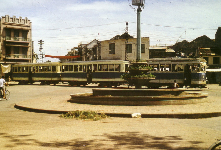 Tàu điện chạy ngang qua đài phun nước ở ngã năm bờ hồ, 1974. Tòa nhà có dòng chữ M.D.Q.D phía trái là mậu dịch quốc doanh. Ảnh: Günter Mosler.