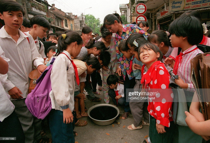 Trẻ em và người lớn hào hứng vây quanh một cái chậu chứa nước pha mực để quan sát hình ảnh phản chiếu của nhật thực ngày 24/10/1995.