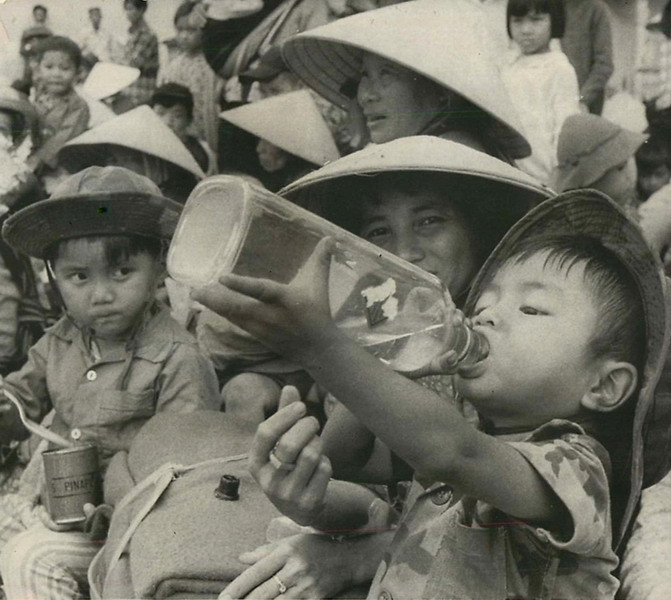 Sau khi phải chịu một cơn khát kéo dài, em bé này tu ừng ực nước đựng trong một chai rượu cũ. Em cùng gia đình đang tập trung tại một sân bóng ở KonTum để chờ được di tản khỏi vùng chiến sự. Ảnh chụp ngày 7/6/1972.