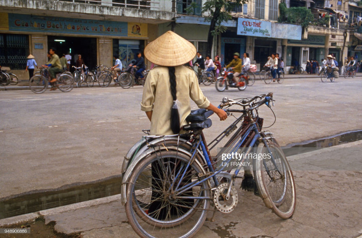 Cô gái ôm ba chiếc xe đạp trên phố Hàng Bài, gần bờ hồ. Một chiếc xe máy hiếm hoi chạy trên con đường toàn xe đạp. Nội dung các bảng hiệu bên kia đường: "Cừa hàng bách hóa phục vụ thiếu nhi", "Thuốc gia truyền Cứu Thế".