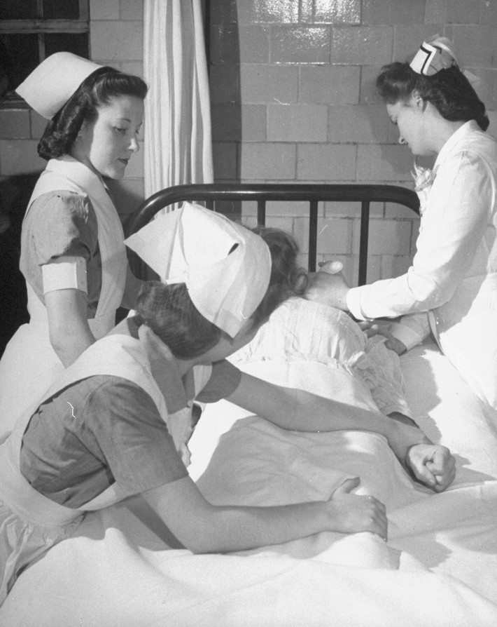 Các y tá khống chế một bệnh nhân đang giãy giụa trên giường.
