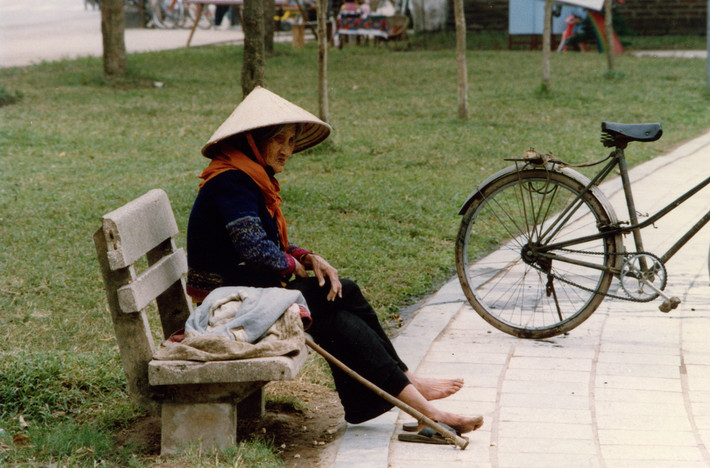 Cụ bà ngồi trên ghế đá bờ hồ.