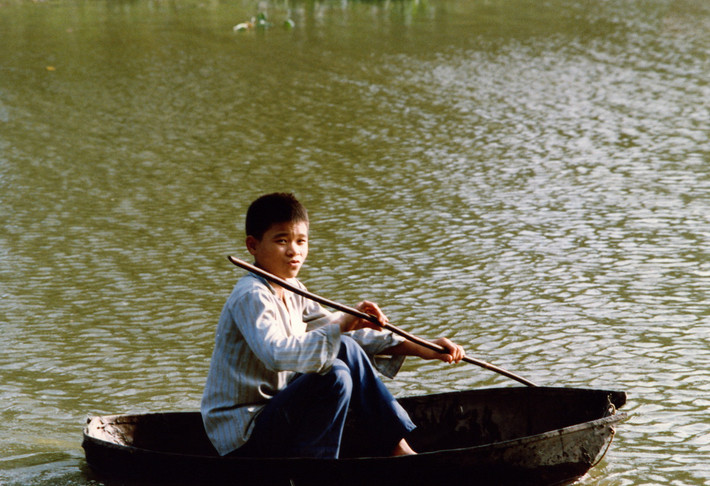 Cậu bé chèo thuyền thúng trên hồ.