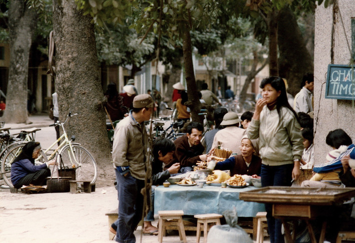 Quán cháo vỉa hè khá đông khách. Gần đó, một cụ bà đang rán bánh chuối và hai mẹ con ngồi trông quầy bán vé số.