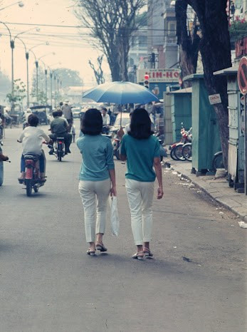 Hai thiếu nữ bước dưới lòng đường vì vỉa hè đã bị các ki-ốt lấn hết, 1968. Ảnh: Brian Wickham