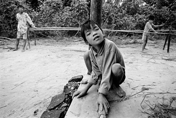 Em Trần Văn Lâm, 10 tuổi, bị chậm phát triển trí não và gặp khó khăn trong đi lại. Hai người anh trai là Trần Văn Thuận và Trần Văn Hoàng cũng có những dị tật ở chân. Cha của các em đã dựng một lối đi bằng tre để giúp các em luyện tập vận động, 1998. Ảnh: Philip Jones Griffiths - Magnumphotos.com