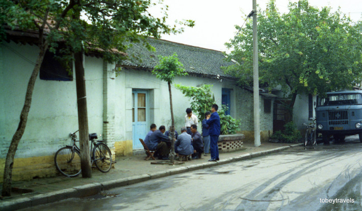 Nhóm nam giới tụ tập trên vỉa hè, dường như là đang đánh cờ.