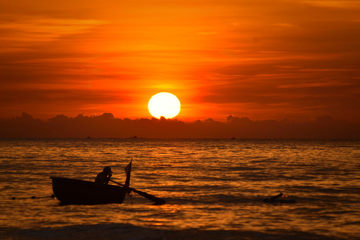 Con thuyền thúng nhỏ bé dưới vầng mặt trời đỏ rực. Ảnh: Raita Futo/ Flickr.