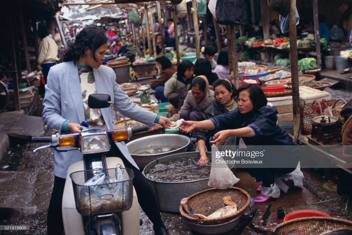 Người phụ nữ ngồi trên xe máy mua tôm cá tại một khu chợ ở Hà Nội.