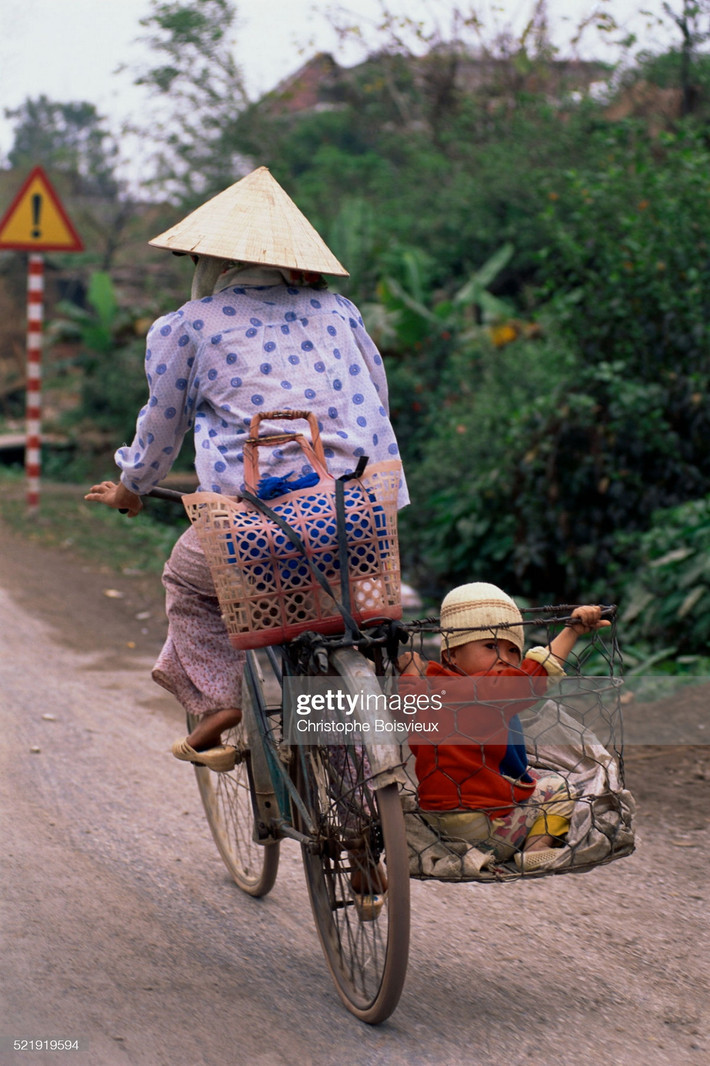 Bà mẹ chở con bằng chiếc sọt sắt gắn sau xe đạp.