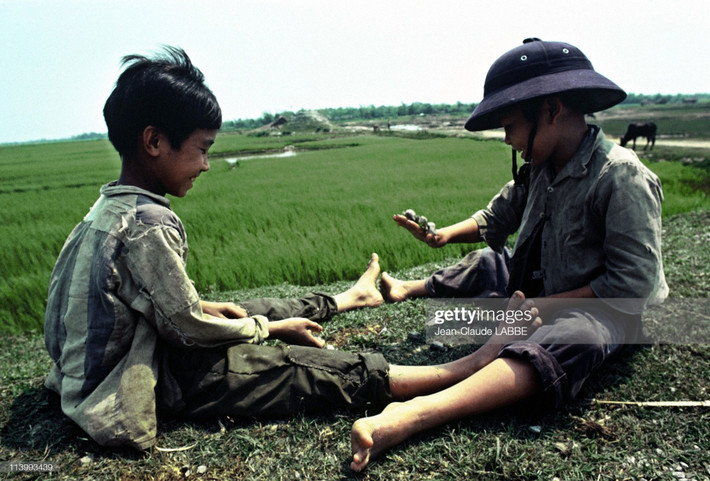 Hai chú bé ngồi chơi trên bờ ruộng.