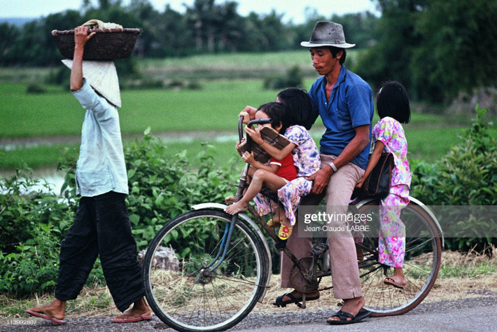 Người đàn ông chở ba đứa trẻ bằng xe đạp trên đường quê.