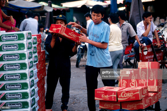 Hai nam giới bốc dỡ các thùng bia Heineken và nước ngọt Coca-Cola tại một khu chợ ở TP HCM, tháng 6/1993. Tại Việt Nam năm 1993, các sản phẩm tiêu dùng phương Tây đã trở nên phổ biến. Ảnh: Paula Bronstein/Getty Images.