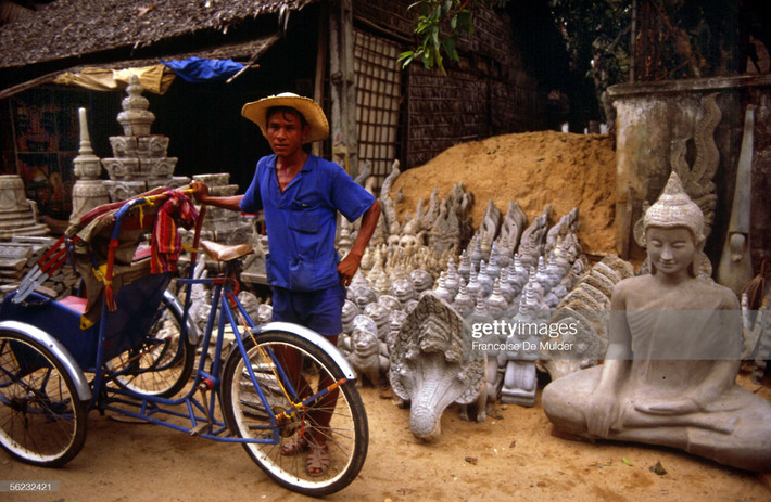 Người lái xích lô đứng bên những bức tượng thờ bày bán ven đường ở Phnom Penh.