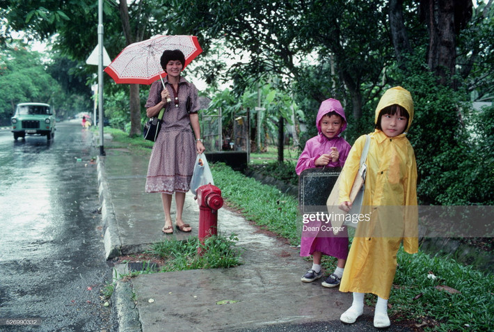 Bà mẹ và hai trẻ nhỏ chờ xe buýt dưới mưa.