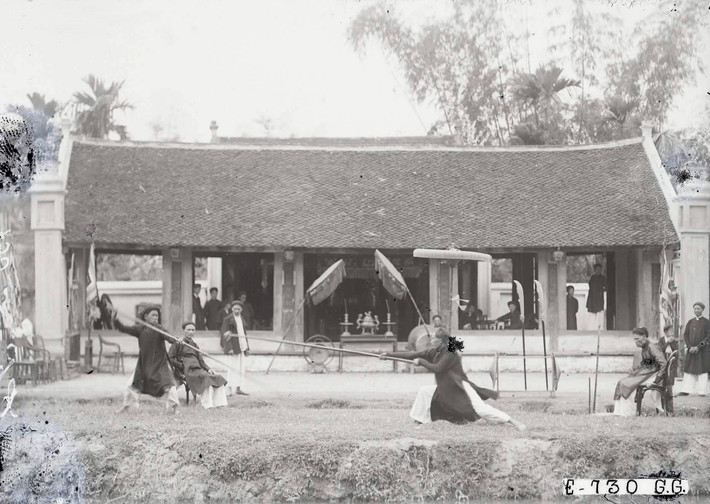 Hai người thi đấu roi trường, trò chơi truyền thống dùng sào gỗ dài bọc vải ở đầu để chiến đầu với nhau trong hội Tết ở tỉnh Hà Đông cũ, 1929.