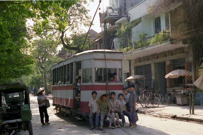 Đám trẻ em ngồi sau toa tàu điện trên phố Quán Thánh, trước hiệu sách nhân dân Ba Đình (ngày nay là hiệu sách Ba Đình, 12 Quán Thánh), Hà Nội năm 1990. Ảnh: Ian Lynas Flickr.