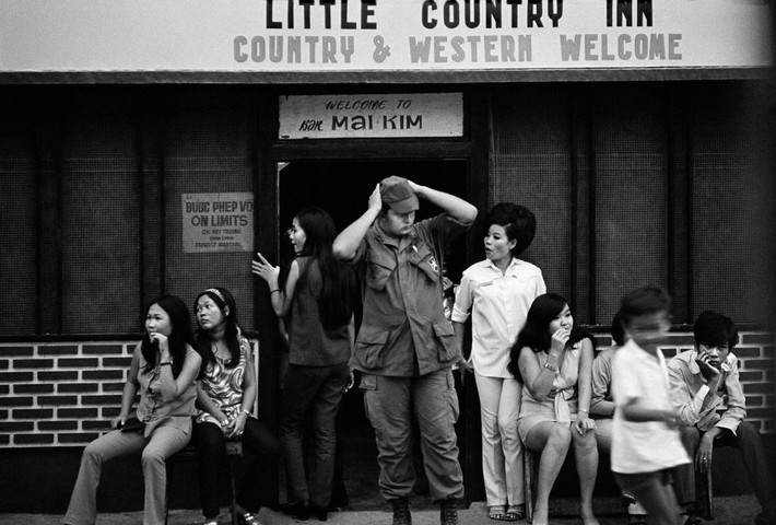 Bên ngoài quán bar Mai Kim ở Cần Thơ, 1970. Ảnh: Philip Jones Griffiths. Phía sau các quán bar phục vụ lính Mỹ là sự bảo kê không chính thức từ giới chức quân đội Sài Gòn.