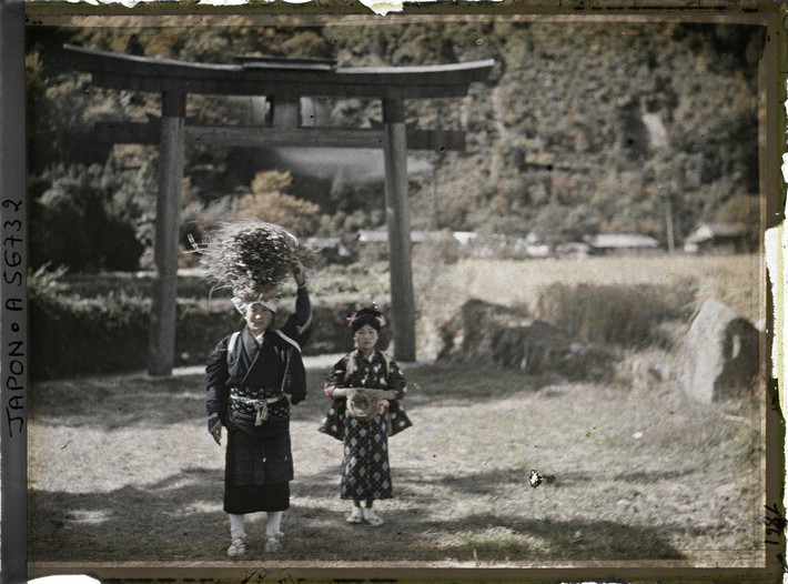 Người phụ nữ và bé gái đứng gần cổng torii của một ngôi đền ở làng Yase.