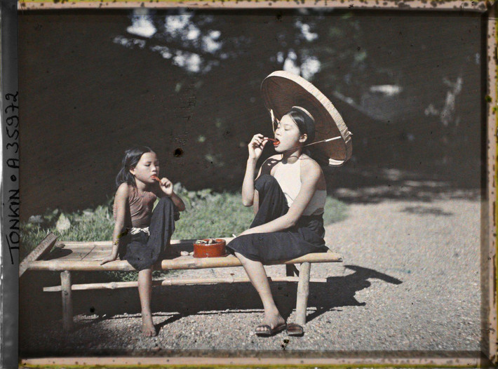 Bé gái và thiếu nữ ngồi trên chõng tre ăn trầu, 1921.