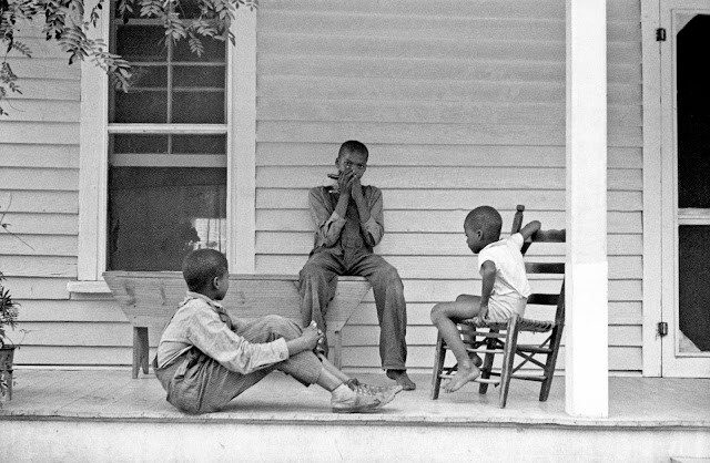 Các cậu bé da màu ngồi chơi bên hiên nhà khi không phải làm việc trên đồng. Ảnh: Arthur Rothstein.
