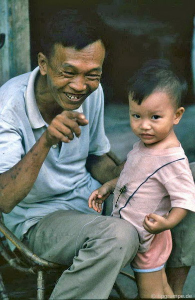 Em bé bên ông nội với chú chuồn chuồn buộc dây làm đồ chơi.