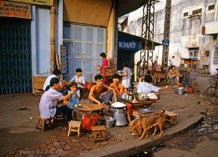 Một chú chó thơ thẩn kiếm ăn tại một quán ăn vỉa hè đầu đường Đề Thám, Sài Gòn năm 1989. Ảnh: Doi Kuro Facebook.
