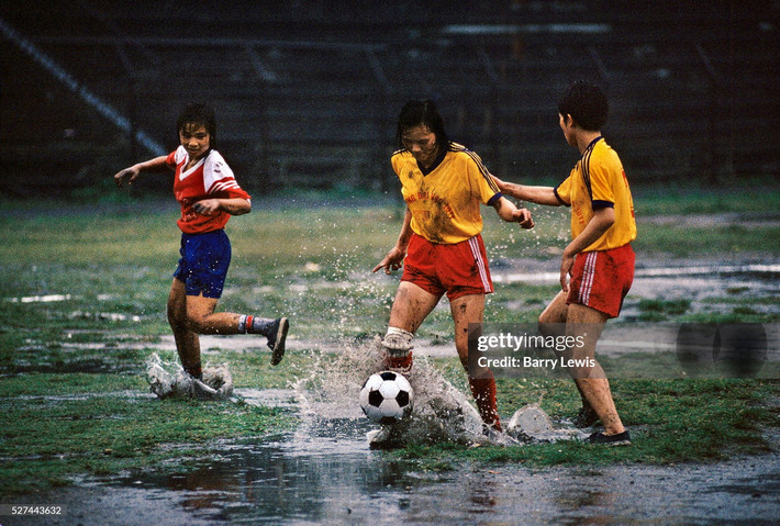 Ba nữ cầu thủ trẻ đá bóng trong cơn mưa lớn ở thị xã Cẩm Phả năm 1997. Gia đình họ làm việc tại các mỏ than ở địa phương. Ảnh: In Pictures Ltd./Corbis via Getty Images.