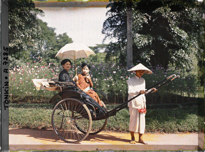 Hai phụ nữ thanh lịch thuộc tầng lớp thượng lưu ngồi trên chiếc xe kéo trong một công viên.